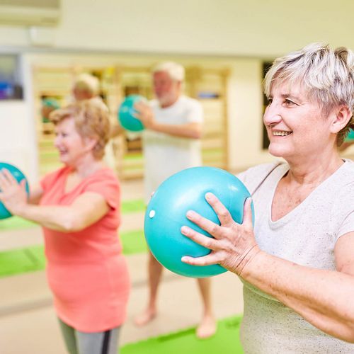 Reha-Patienten heben einen Gymnastikball vor die Brust, um Herzinsuffizienz vorzubeugen