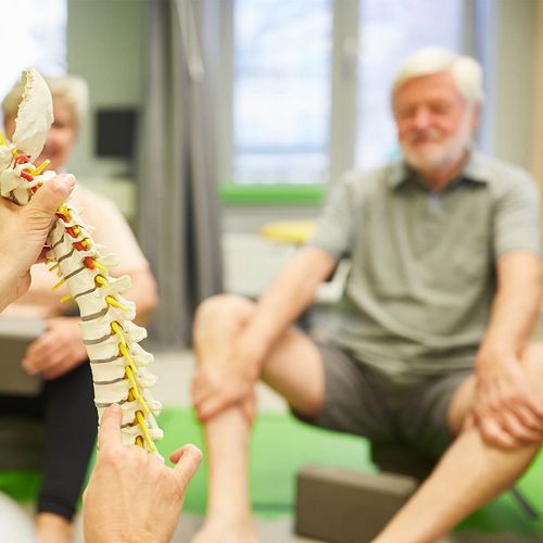 Rehaübungsleiter erklärt Reha-Patienten anhand eines Skelettmodells Osteoporose