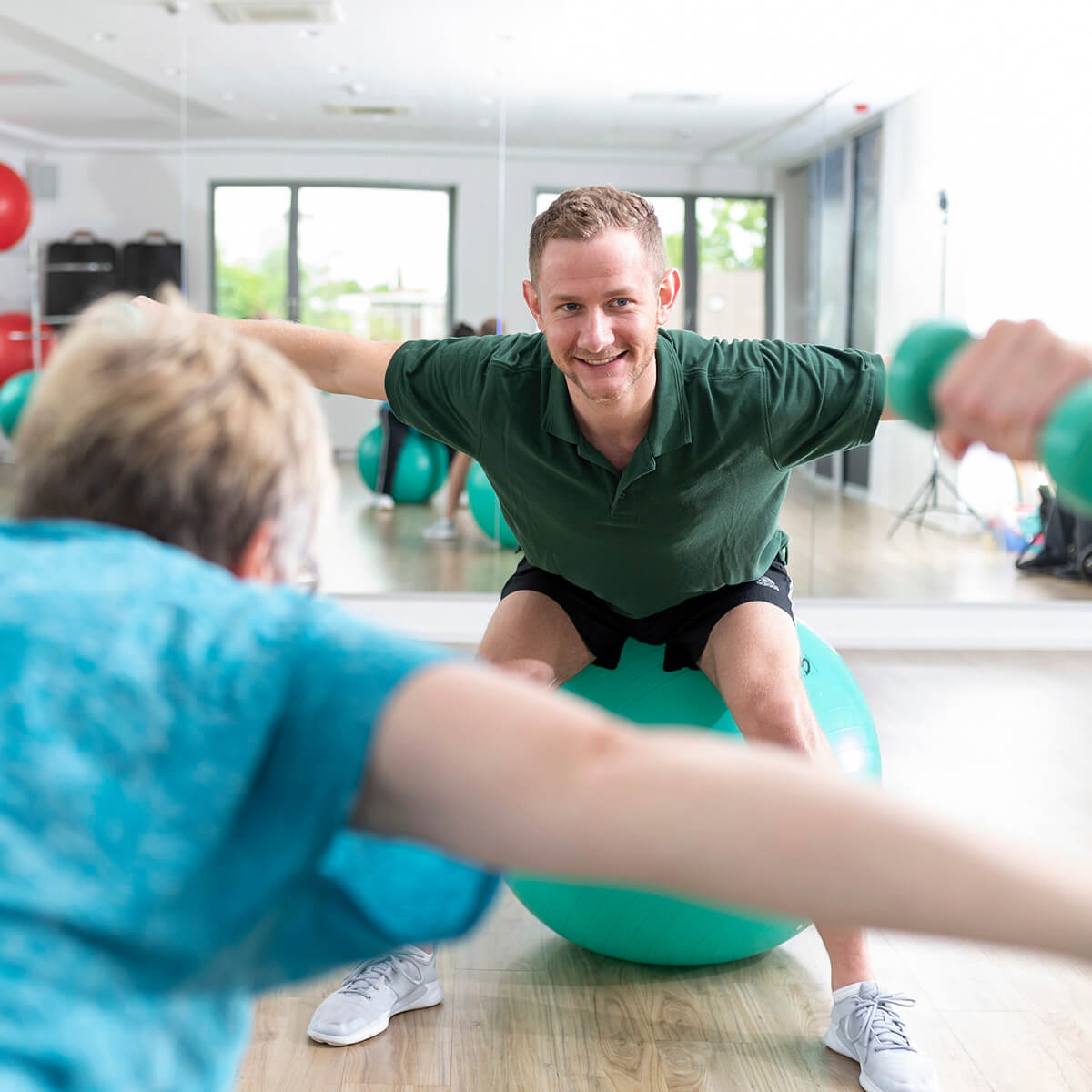 Reha-Patientin mit Übungsleiter beim Rückensport in Form von Übungen mit Hanteln